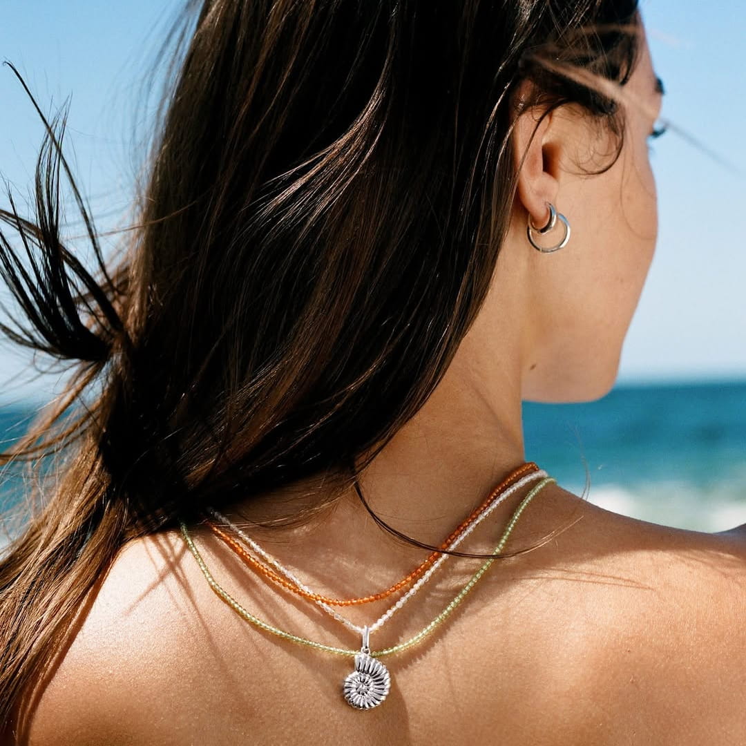 Model wearing layered gold necklaces with a medallion pendant, outdoor lifestyle shot